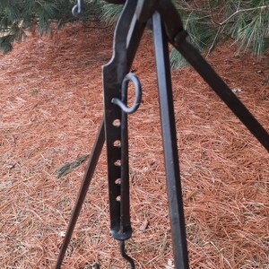 Peut inclure: Un tr&eacute;pied en m&eacute;tal noir avec un crochet et une boucle d&eacute;corative. Le tr&eacute;pied est pos&eacute; sur un lit d'aiguilles de pin.