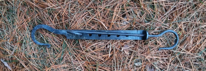 Peut inclure: Un crochet en m&eacute;tal noir avec une longue barre fine et deux crochets &agrave; chaque extr&eacute;mit&eacute;. La barre comporte cinq trous espac&eacute;s uniform&eacute;ment sur toute sa longueur.