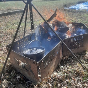 Peut inclure: Une marmite en fonte noire suspendue au-dessus d'un foyer avec un tr&eacute;pied en m&eacute;tal. Le foyer est en m&eacute;tal et porte les mots "Buchraun" et "Uncle Buck's Forge" grav&eacute;s dans le m&eacute;tal.