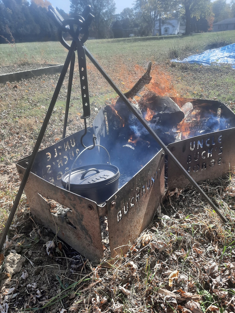 Peut inclure: Une marmite en fonte noire suspendue au-dessus d'un foyer avec un tr&eacute;pied en m&eacute;tal. Le foyer est en m&eacute;tal et porte les mots "Buchraun" et "Uncle Buck's Forge" grav&eacute;s dans le m&eacute;tal.