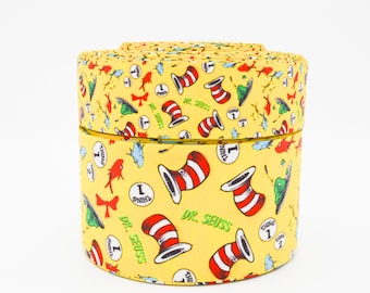 May include: A yellow ribbon roll featuring a repeating pattern of Dr. Seuss characters and imagery. The design includes the Cat in the Hat's hat, Thing 1, and other whimsical elements. The ribbon is rolled and presented in a cylindrical shape.