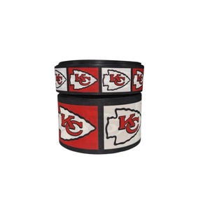 May include: Red, white, and black ribbon with a repeated pattern of the Kansas City Chiefs logo. The logo features an arrowhead with the letters "KC" inside.