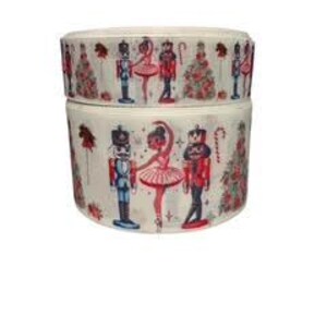 May include: Two rolls of decorative washi tape featuring a festive Nutcracker theme. The tape showcases illustrations of nutcrackers, ballerinas, and Christmas trees in red, blue, and green on a cream background. Each roll is stacked on top of each other.