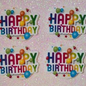 May include: Four colorful Happy Birthday cake toppers with a rainbow design and balloons. The toppers are on a sparkly pink background.