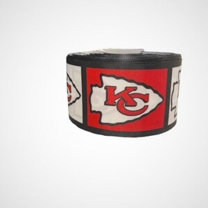 May include: A black and red ribbon with a white arrowhead and the letters "KC" in red. The arrowhead is a common symbol for the Kansas City Chiefs.