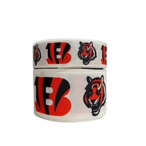 May include: White ribbon with a black and orange Cincinnati Bengals logo and a tiger head. The ribbon is rolled up and ready to be used for crafts or decorations.