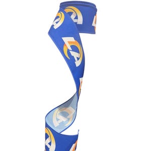 May include: A blue ribbon with a repeating pattern of the LA Rams logo in white, yellow, and orange. The ribbon is curled and displayed against a white background. This decorative ribbon is suitable for crafts and gift wrapping.