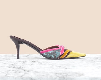 May include: A pair of colorful heeled mules with a pointed toe. The shoes are made of a combination of materials, including snakeskin, velvet, and leather. The heels are a medium height and the shoes have a bright yellow, pink, and blue color scheme.