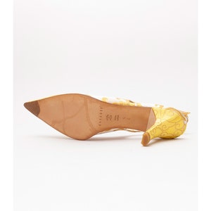 Puede incluir: Sandalias de tac&oacute;n amarillo y blanco con estampado floral. Las sandalias tienen punta puntiaguda y tac&oacute;n fino. La suela del zapato es de cuero marr&oacute;n con el nombre de la marca "Casadei" impreso en ella.