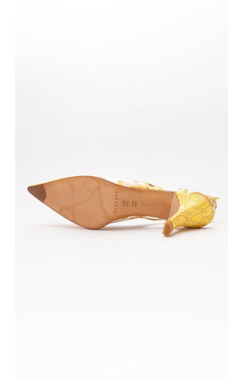 Puede incluir: Sandalias de tac&oacute;n amarillo y blanco con estampado floral. Las sandalias tienen punta puntiaguda y tac&oacute;n fino. La suela del zapato es de cuero marr&oacute;n con el nombre de la marca "Casadei" impreso en ella.