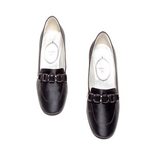 May include: A pair of black satin loafers featuring a rounded toe and a decorative strap across the vamp adorned with rectangular black crystals. The interior lining is white with the text Casadei printed inside an oval frame on the insole.