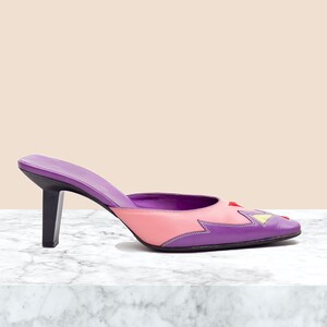 May include: Purple and pink leather heeled mules with a geometric design on the toe. The heels are about 3 inches tall.