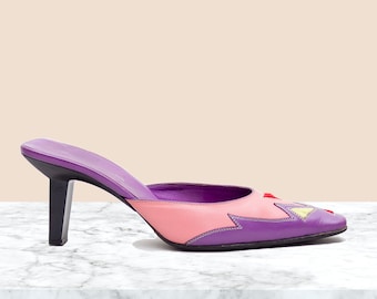 May include: Purple and pink leather heeled mules with a geometric design on the toe. The heels are about 3 inches tall.