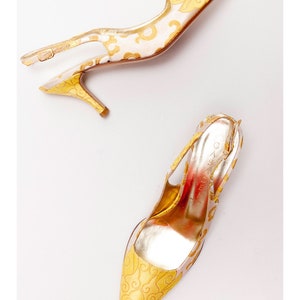 Puede incluir: Un par de zapatos de tac&oacute;n alto amarillos y dorados con un patr&oacute;n floral. Los zapatos tienen una punta puntiaguda y un tac&oacute;n delgado.