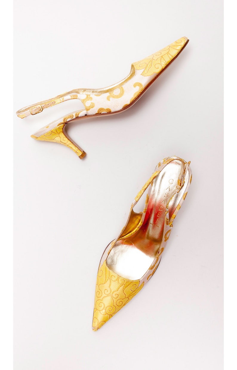 Puede incluir: Un par de zapatos de tac&oacute;n alto amarillos y dorados con un patr&oacute;n floral. Los zapatos tienen una punta puntiaguda y un tac&oacute;n delgado.