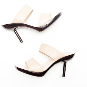May include: Two pairs of beige heeled sandals with black straps and black heels. The sandals are on a white background.