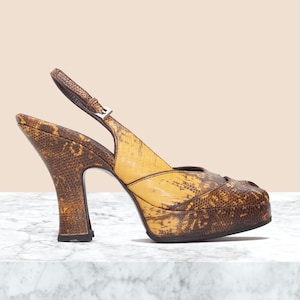 May include: A slingback platform high heel shoe featuring a textured brown and yellow snakeskin pattern. The shoe has a peep-toe front, a thick platform sole, a flared heel, and an adjustable ankle strap with a small silver-toned metal buckle.