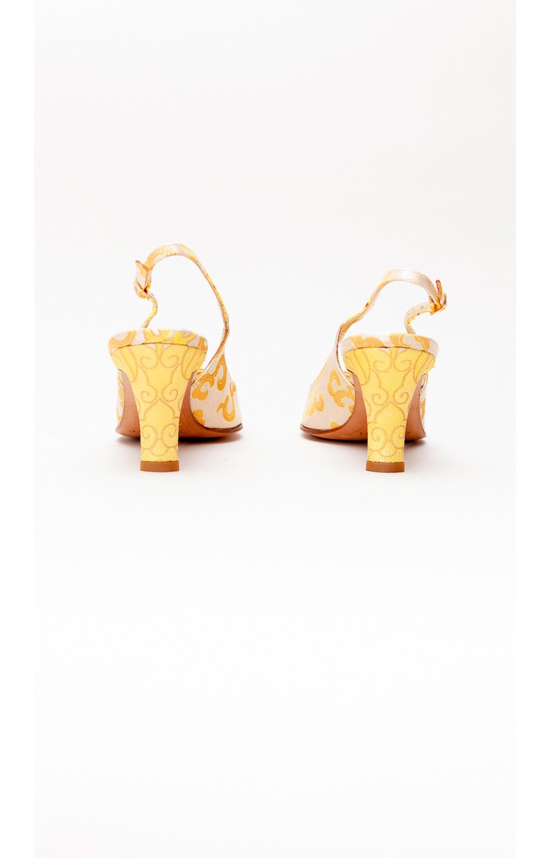 Puede incluir: Un par de tacones amarillos y blancos con tira en el tobillo y un estampado floral. Los tacones miden aproximadamente 7,5 cm de alto.