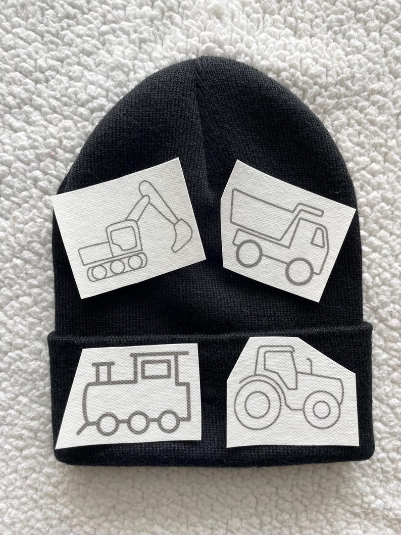 May include: Black beanie with four white patches featuring outlines of a tractor, a dumper truck, an excavator, and a train. The patches are blank and ready to be coloured in.