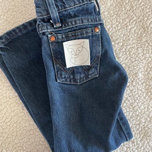 May include: A pair of dark blue denim jeans with a white patch on the back pocket featuring a black outline of a fox.