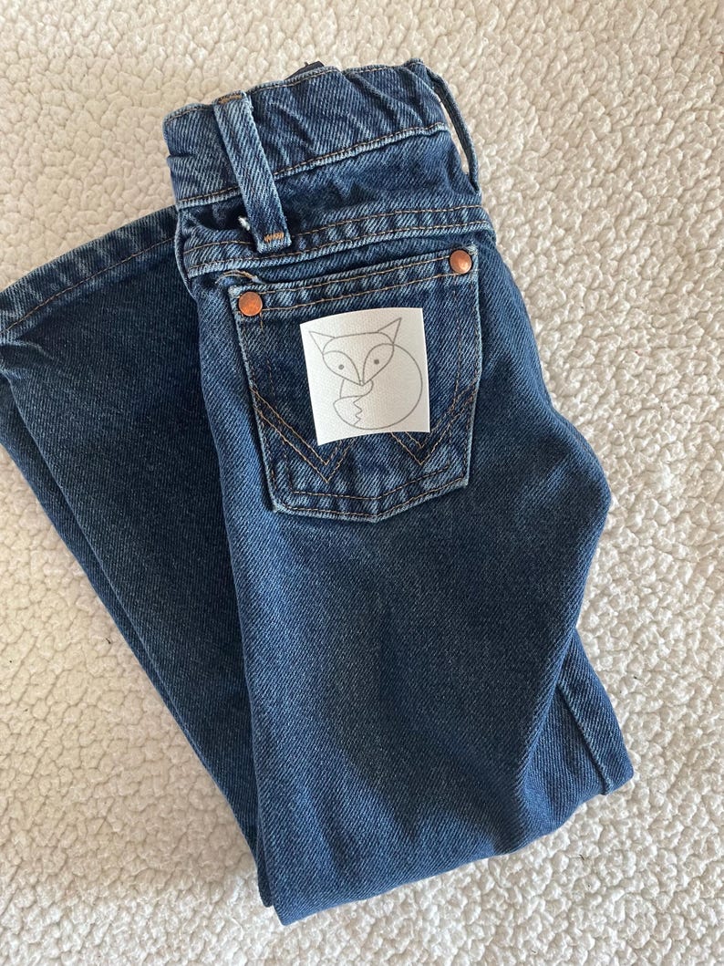 May include: A pair of dark blue denim jeans with a white patch on the back pocket featuring a black outline of a fox.