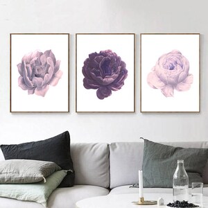 Puede incluir: Tres impresiones enmarcadas de flores moradas y rosas. Las impresiones est&aacute;n dispuestas en una fila en una pared blanca sobre un sof&aacute; gris.