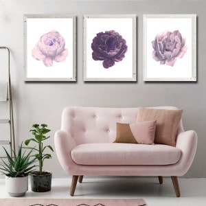 Puede incluir: Tres impresiones enmarcadas de flores moradas y rosas. Las impresiones est&aacute;n en marcos blancos y est&aacute;n colgadas en una pared blanca sobre un sof&aacute; rosa.