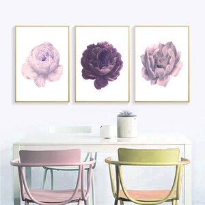 Puede incluir: Tres impresiones enmarcadas de flores moradas y rosas. Las impresiones est&aacute;n en marcos dorados y est&aacute;n colgadas en una pared blanca. Las impresiones est&aacute;n sobre una mesa blanca con dos sillas.
