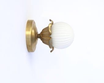 Op de afbeelding: Een vintage wandlamp met een messing afwerking. De lamp heeft een ronde basis, een decoratieve bloemvormige steun en een witte, geribbelde glazen bol. De armatuur is ontworpen voor wandmontage en zorgt voor sfeerverlichting.