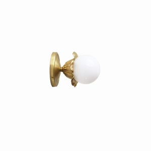 May include: A brass wall sconce with a white globe-shaped light bulb. The sconce features a round base and a decorative floral design around the bulb. The fixture is designed for indoor lighting.