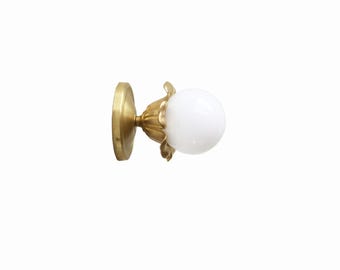 May include: A brass wall sconce with a white globe-shaped light bulb. The sconce features a round base and a decorative floral design around the bulb. The fixture is designed for indoor lighting.