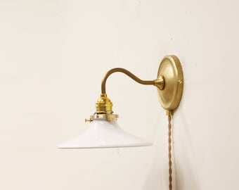 May include: A white porcelain lampshade with a brass arm and wall mount. The lampshade is angled downwards and has a simple, modern design.