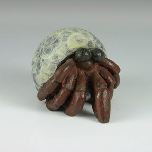 May include: A ceramic hermit crab figurine with a white and gray shell and brown legs. The figurine is a decorative object.
