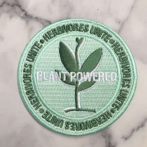 May include: A green embroidered patch with a white plant design and the text "PLANT POWERED" surrounded by the text "VEGANORES UNITE + HERBIVORES UNITE + VEGANORES UNITE + HERBIVORES UNITE"