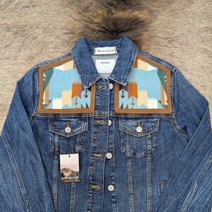 May include: A blue denim jacket with a decorative patch on the shoulders. The patch features a geometric design in shades of blue, brown, and cream. The jacket has a button-up front, two chest pockets, and the Old Navy label.