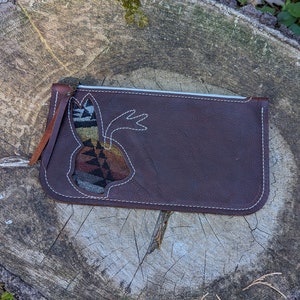 May include: A brown leather zippered pouch with a cut-out design of a rabbit. The rabbit is filled with a colorful patterned fabric.