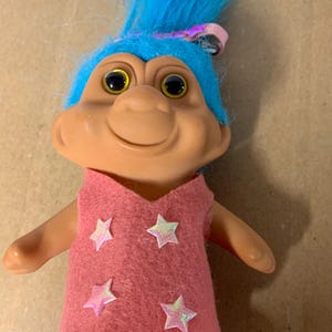 11 cm TNT Troll Puppe 1991 mit blauen Haaren, Haarspange, gelben Augen und handgenähtem rosa Filzkleid mit rosa Sternen
