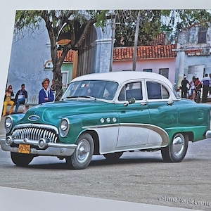 May include: A vintage green and white car parked on a street in a town. The car has a chrome bumper and a license plate that reads "P-1504".