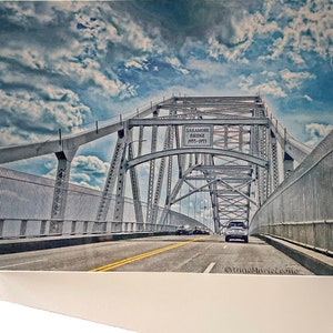May include: A view of the Sagamore Bridge in Massachusetts, a steel arch bridge with a sign that reads "Sagamore Bridge 1935-1973". The bridge is over a body of water and there are cars driving on the bridge.