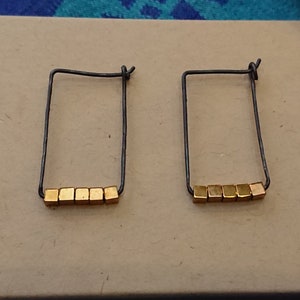 May include: A pair of gold and black hoop earrings with a row of small gold cube beads on each hoop.