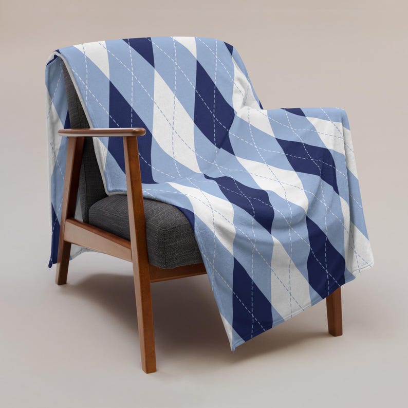 May include: A blue, white, and navy argyle patterned throw blanket draped over a wooden armchair. The blanket features a repeating diamond design with white stitching. The chair has a gray seat and back.