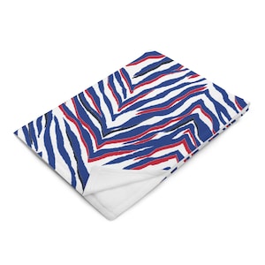 May include: A white, blue, and red zebra print throw blanket. The blanket is folded and the pattern is visible on the top side.