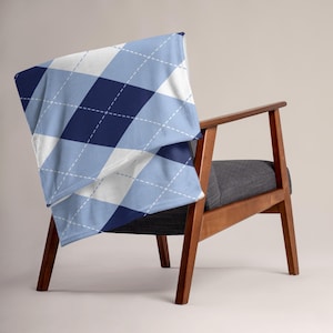 May include: A throw blanket with a blue, white, and navy argyle pattern draped over a wooden chair with a gray seat. The blanket features a diamond design with white stitching.