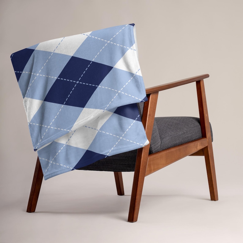 May include: A throw blanket with a blue, white, and navy argyle pattern draped over a wooden chair with a gray seat. The blanket features a diamond design with white stitching.