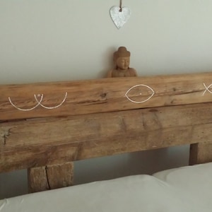 Könnte beinhalten: Ein hölzernes Kopfteil mit weißen, gemalten Designs von Brüsten, Augen und Fischen. Das Kopfteil ist aus wiederverwendetem Holz gefertigt und hat einen rustikalen Look.