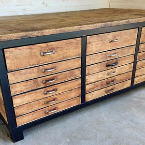 Könnte beinhalten: Ein großer industrieller Schrank aus wiederverwendetem Holz mit schwarzem Metallrahmen und mehreren Schubladen. Der Schrank hat eine dicke Holzplatte und ist aus recyceltem Holz gefertigt.