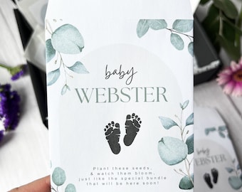 May include: A white envelope with a watercolor design of eucalyptus leaves and a baby footprint. The envelope has the text "baby WEBSTER" and "Plant these seeds, & watch them bloom, just like the special bundle that will be here soon!"