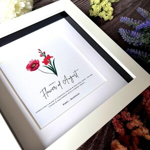 May include: A white framed print with a red poppy and a pink gladiolus flower illustration. The text reads "You're a Flower of August, symbolizing a blend of strength, passion & emotional depth. You are strong & independent with a vibrant energy. Poppy - Gladiolus"