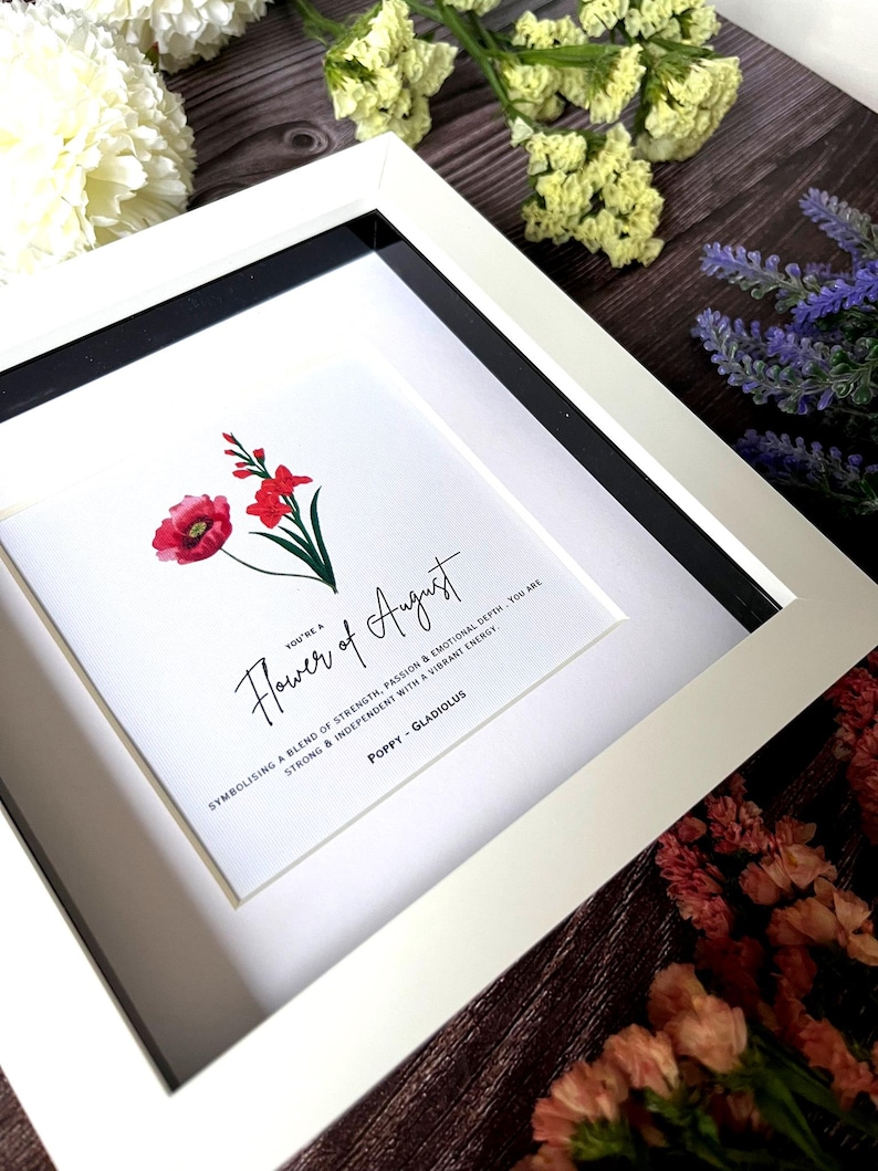 May include: A white framed print with a red poppy and a pink gladiolus flower illustration. The text reads "You're a Flower of August, symbolizing a blend of strength, passion & emotional depth. You are strong & independent with a vibrant energy. Poppy - Gladiolus"