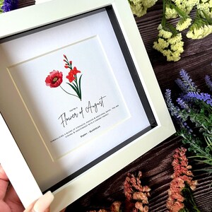 May include: A white frame with a white mat and a print of a red poppy and a pink gladiolus. The print has the text "You're a Flower of August" and "Symbolising a blend of strength, passion & emotional depth. You are strong & independent with a vibrant energy. Poppy - Gladiolus."